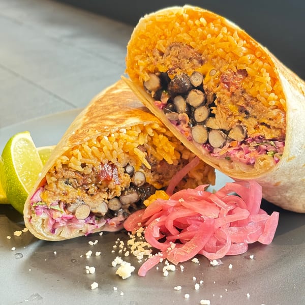 Two halves of a Flyin Taco burrito, filled with rice, beans, and meat, with pickled onions and lime.