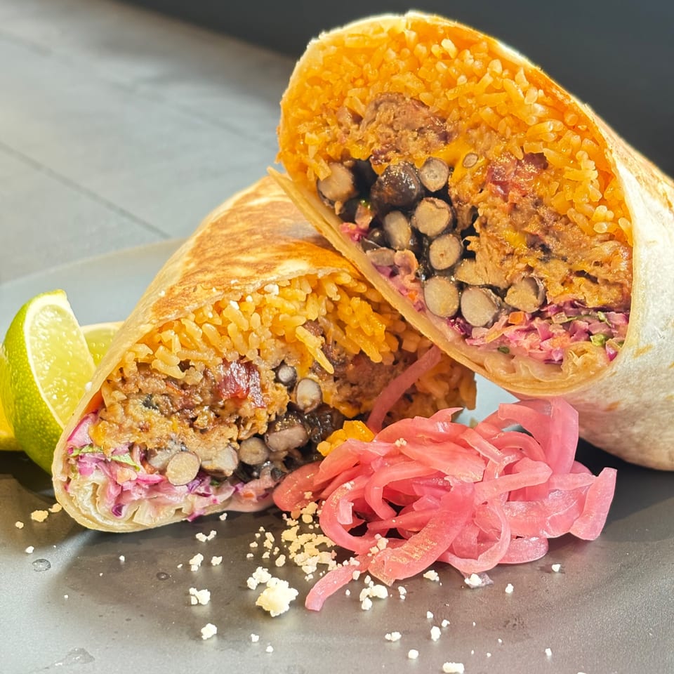 Two halves of a Flyin Taco burrito, filled with rice, beans, and meat, with pickled onions and lime.