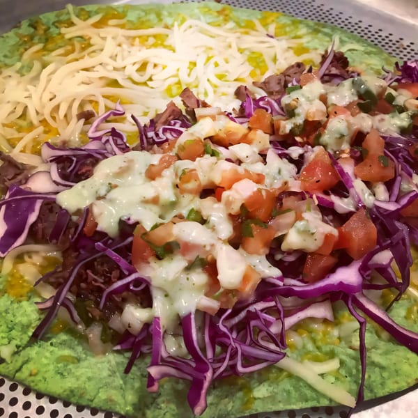 A large green tortilla filled with shredded cheese, meat, purple cabbage, pico de gallo, and a creamy sauce.