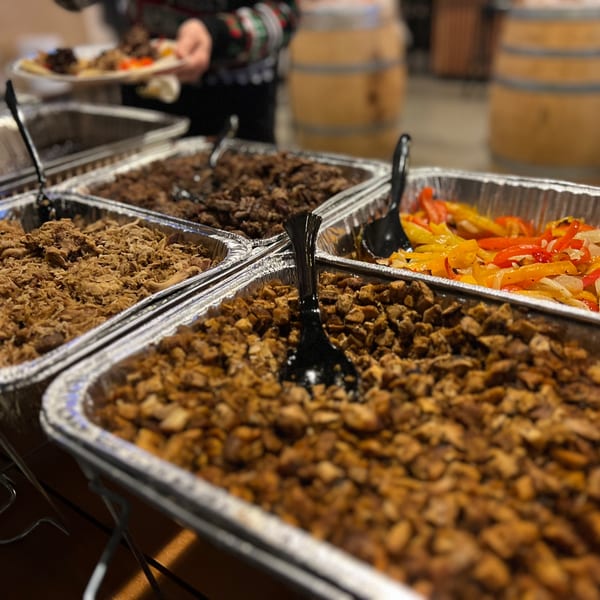 A catering spread of Mexican food, including shredded chicken, beef, and fajita vegetables.