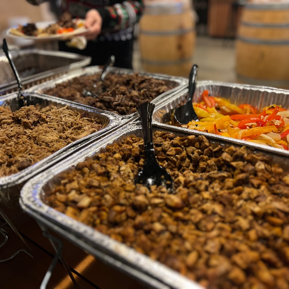 A catering spread of Mexican food, including shredded chicken, beef, and fajita vegetables.