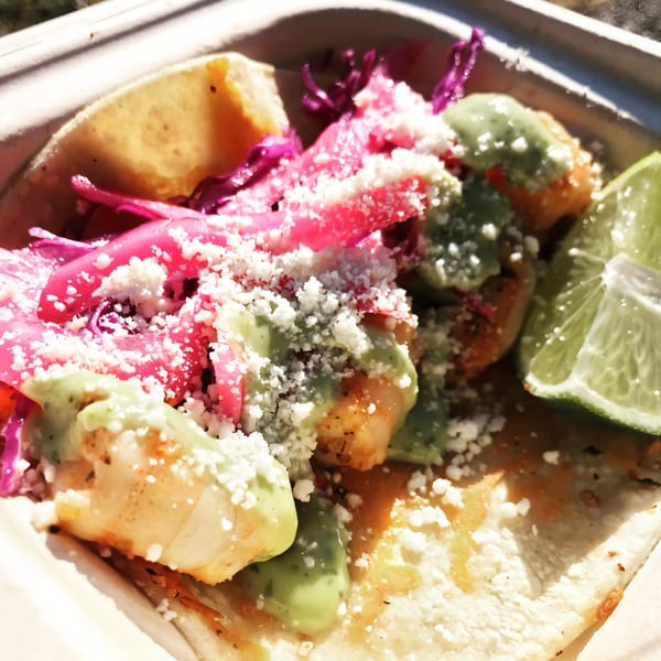 Close-up of a Flyin Taco shrimp taco with pink pickled onions, green sauce, and cotija cheese.