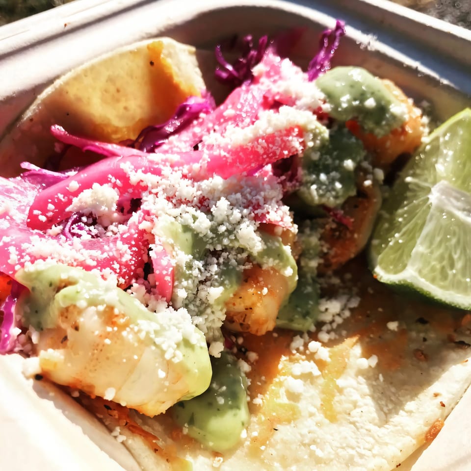 Close-up of a Flyin Taco shrimp taco with pink pickled onions, green sauce, and cotija cheese.